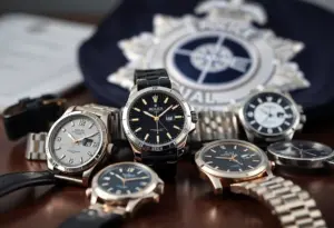Luxury watches on a table with a police badge in the background.