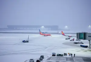 Airport operations disrupted by winter storm showing snow on runways and de-icing crews.